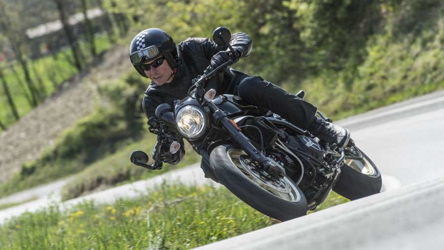 A black Ducati Scrambler Café Racer 2017 being ridden on a rural road